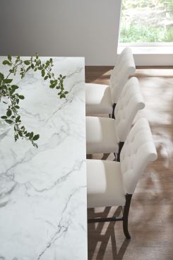 Luxurious bar chairs with tufted fabric seats and dark wood frames aligned along a marble kitchen island.