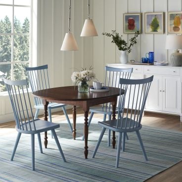 Cozy breakfast nook featuring an elegant oval dining table with turned legs, paired with classic spindle-back chairs in a soft blue finish.