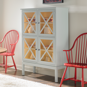 A cozy dining nook featuring a light blue glass-front cabinet with crossed wood detailing, complemented by bold red Windsor chairs.