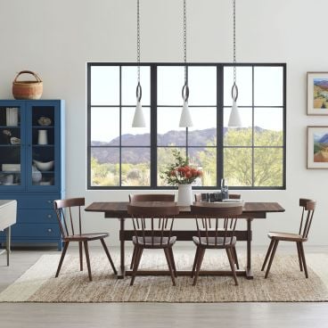 Dining room with a dark wood trestle table, spindle-back chairs, a blue glass-front cabinet, and large windows showcasing a scenic mountain view.