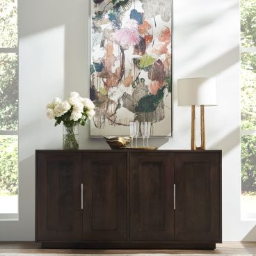 A dark wood buffet with a rich finish, adorned with a large abstract painting, flanked by a modern lamp and a vase of white flowers.