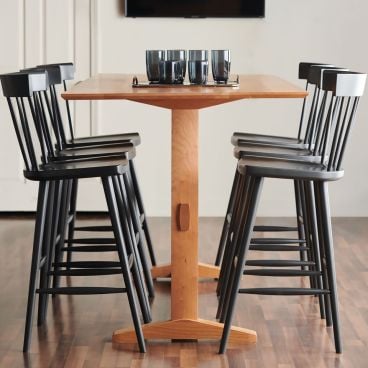 Cherry wood pub table with black spindle-back bar stools, perfect for casual dining or entertaining in modern spaces.