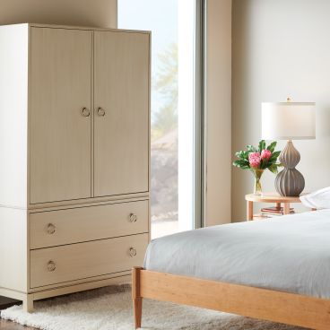 A modern bedroom featuring a handcrafted wooden bed frame and a light-finished wooden armoire with brass ring handles for stylish storage.