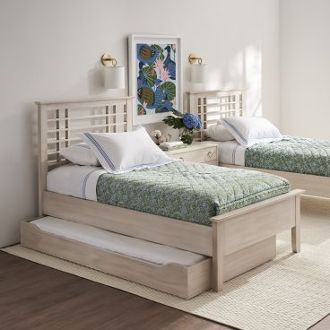 Twin beds with a trundle bed, featuring light wood headboards and green bedding, set in a bright room with large windows overlooking a garden.