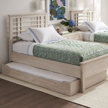 A pair of twin beds with matching light wood frames and green quilts, featuring a trundle bed beneath one bed, in a serene bedroom.