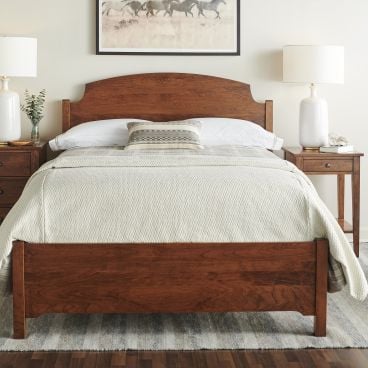 A classic solid wood bed with a gracefully curved headboard and footboard, accompanied by matching wooden nightstands and soft neutral bedding.