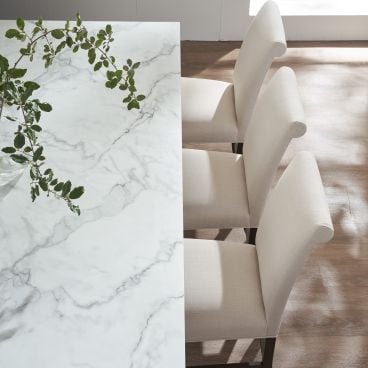Dining chairs with upholstered backs and seats arranged alongside a sleek, marble-topped table, highlighting a blend of modern and traditional design.