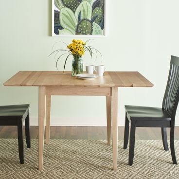 Solid wood drop-leaf dining table with a light natural finish, paired with black spindle-back chairs in a modern dining setting.