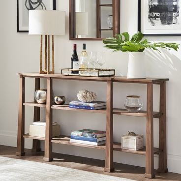 Craftsman-style wood console table with decorative items and books, complemented by a sleek mirror and table lamp.