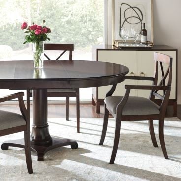A handcrafted solid wood round dining table with a pedestal base, paired with X-back armchairs for a timeless and elegant dining space.