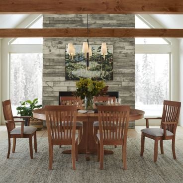 Warm and inviting solid wood round dining table with slatted-back chairs in a cozy winter lodge setting