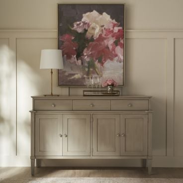Sophisticated server made with real Appalachian hardwood in a light wood finish, featuring drawers and cabinets, complemented by a table lamp and a vibrant floral artwork above.