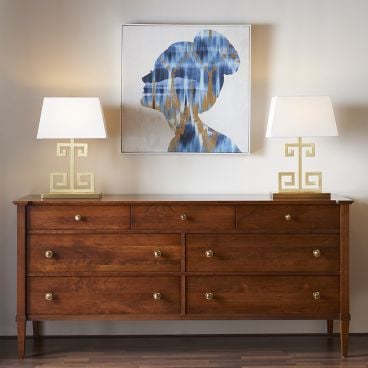A beautifully crafted wooden dresser with sleek brass hardware, complemented by artistic table lamps and a modern framed silhouette painting above.