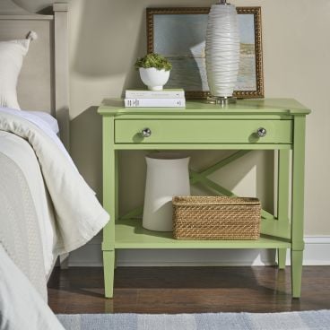 Painted solid wood nightstand in fresh green beside a bed, styled with a white lamp, small plant, and framed coastal artwork.
