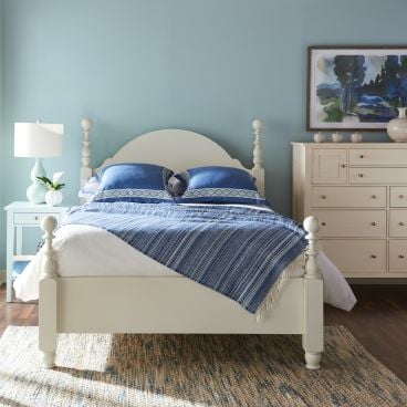 A real wood four-poster bed featuring an arched headboard and classic turned details, crafted from sustainably sourced hardwood.