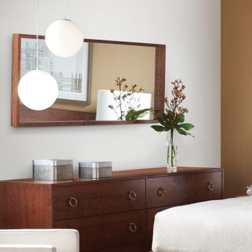 A rectangular wooden-framed mirror mounted above a dark wood dresser, reflecting a stylish and modern bedroom setting.