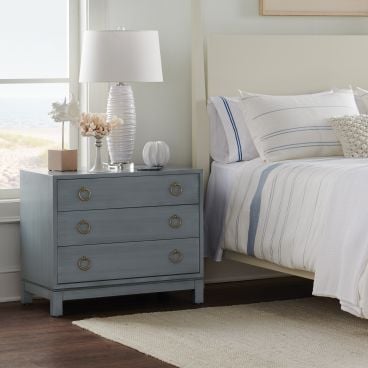 Three-drawer solid wood nightstand in a soft blue finish, styled in a coastal-inspired bedroom.