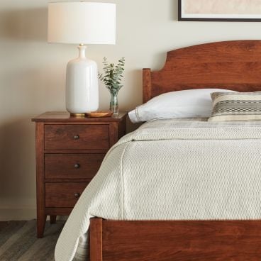 A handcrafted solid cherry wood bed with a curved headboard, accompanied by matching nightstands and a tall dresser for a cohesive bedroom set.