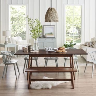 Scandinavian-style dining room with a sleek wood dining table, matching bench, and pastel spindle-back chairs, complemented by natural light and minimalist decor.
