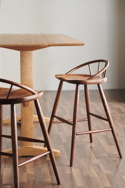 Wooden pub-height dining table paired with sleek, curved wooden bar stools featuring spindle backrests, perfect for modern dining spaces.