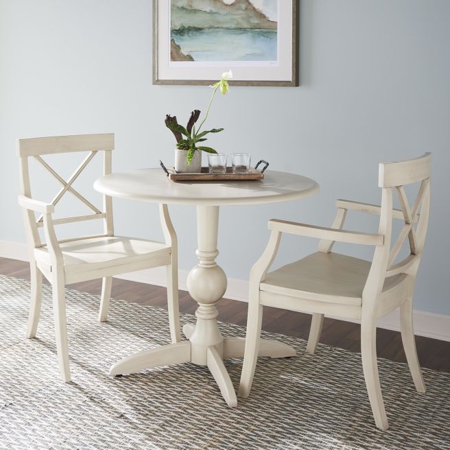 Elegant round pedestal dining table with two X-back solid wood chairs in a hand-glazed finish, creating a timeless breakfast nook.