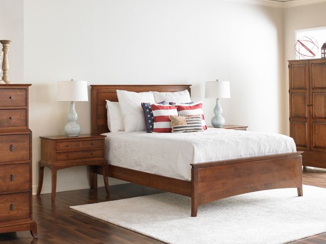 Traditional solid cherry wood nightstand with graceful legs and practical storage, beautifully styled in a bedroom setting with a panel bed and decorative accents.