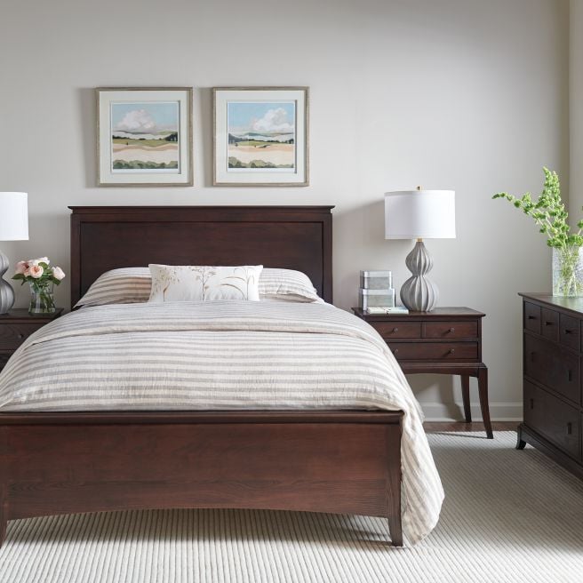 aditional style bedroom featuring a solid wood bed frame in a dark finish with striped bedding and two landscape paintings above.