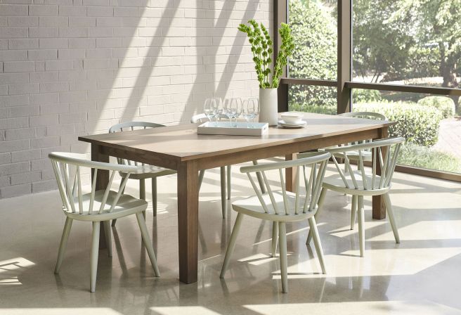 A solid wood dining table with chairs and a vase with a plant on it.