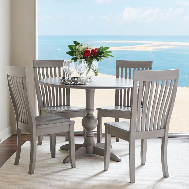 Round solid wood dining table with a classic pedestal base and matching chairs in a refined gray finish