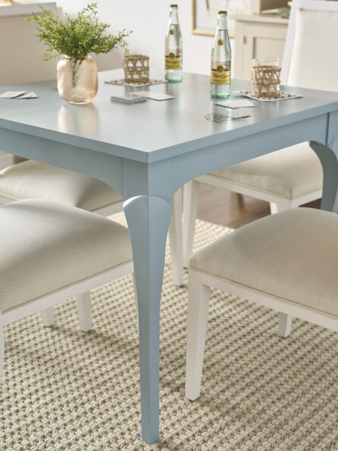 Detail of a small painted wood dining table and cream fabric chairs set for cards and drinks.