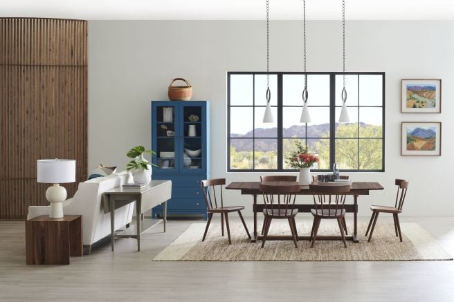 Modern dining room featuring a wooden dining chair set around a natural wood table, complemented by a blue cabinet and scenic window views.