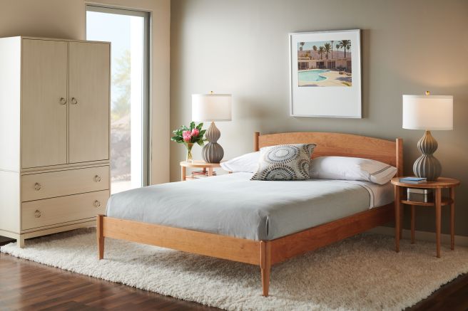 A serene bedroom with a minimalist wooden bed, a neutral-toned armoire with spacious drawers, and a cozy bedside table with a decorative lamp and fresh flowers.