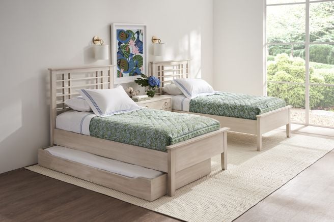 Twin beds with solid wood frames and green patterned quilts in a bright, featuring a roll away bed in a minimalist bedroom with large windows.