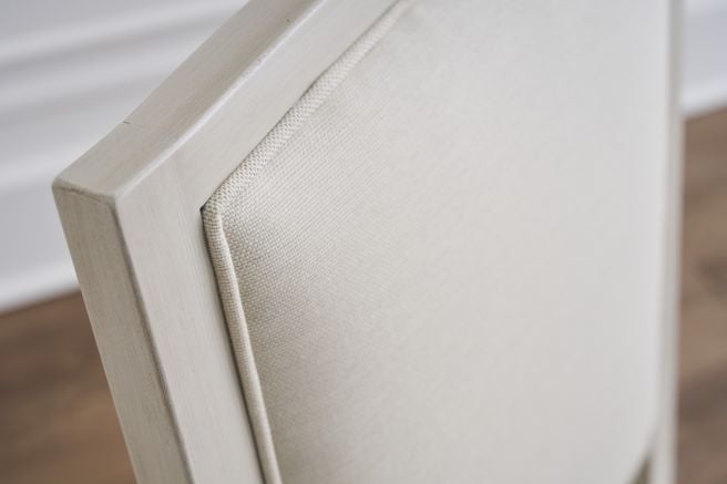 Close up of an upholstered dining chair back with a light solid wood frame and finely textured fabric.