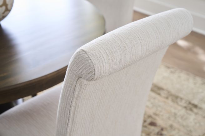 Textured fabric on the rolled top of an upholstered dining chair, part of a solid wood dining set.
