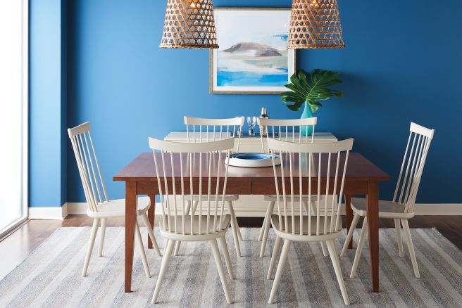 A modern dining setup with a handcrafted wooden table and white spindle chairs, complemented by woven pendant lights and coastal-inspired decor.