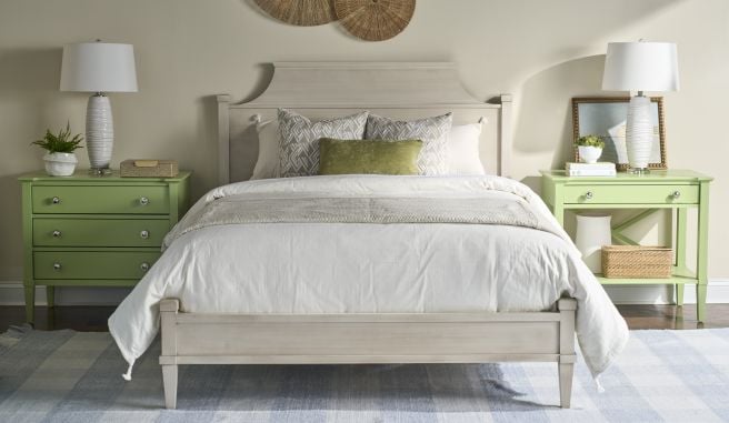 Solid wood bed framed by two nightstands with lamps, styled with layered bedding and accent pillows in a bright bedroom.