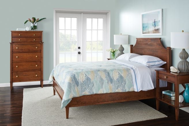 Solid wood bed frame and matching nightstand with French doors in the background, styled in a serene bedroom.