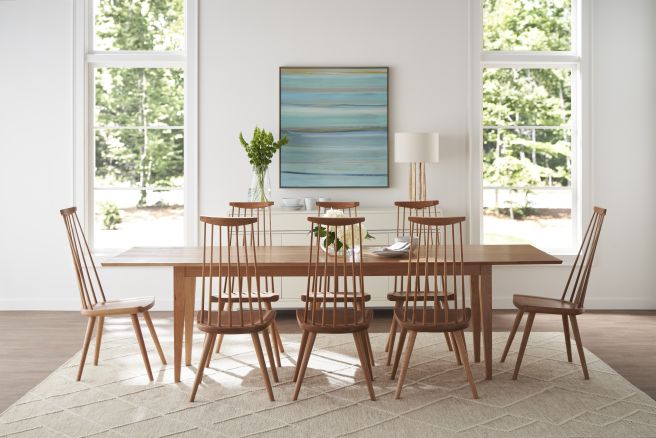 Modern dining room featuring a wooden table with eight spindle-back chairs, set against large windows and a white buffet.