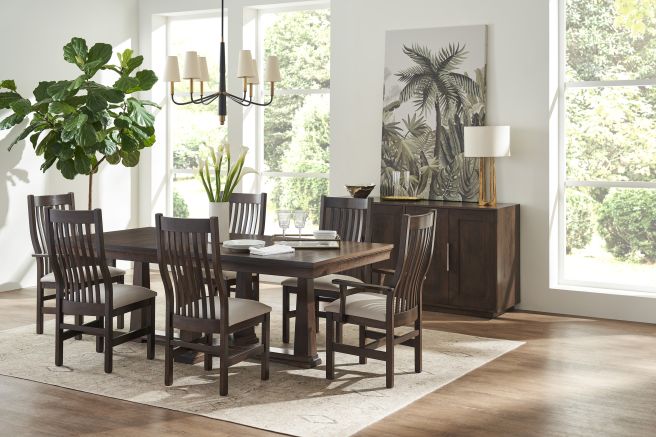 Modern dining room with a dark wood trestle table and slatted-back chairs, complemented by a stylish sideboard and greenery.