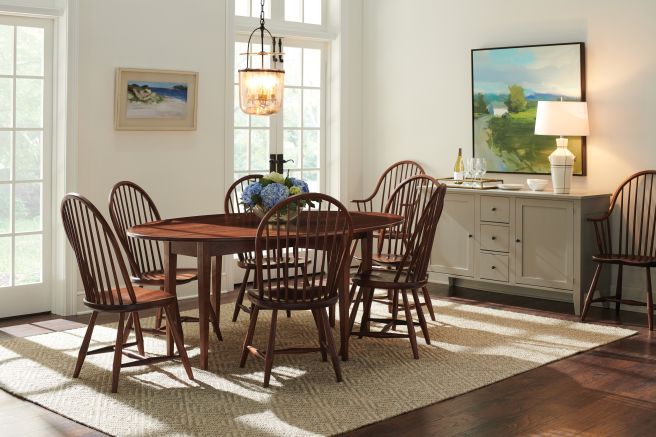 Classic dining room featuring Windsor chairs and an oval wooden table, illuminated by a rustic pendant light with natural light streaming in.