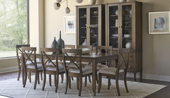 Rectangular hardwood table with eight chairs on a patterned rug, framed by twin china cabinets and modern pendant lighting.