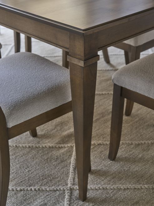 Detail of a hardwood dining table base and legs, surrounded by cushioned dining chairs in a modern dining room.