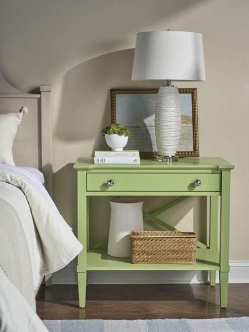 Fresh green hardwood bedside table with drawer and lower shelf, holding a lamp, plant, and woven storage basket.