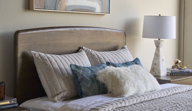 Detail of a hardwood bed headboard showing smooth grain and layered bedding with blue patterned pillows in a modern bedroom.