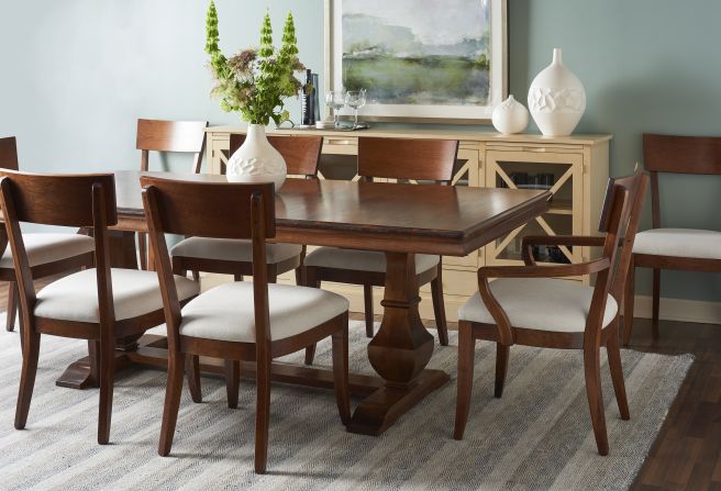 Elegant dining room featuring a solid wood dining table with pedestal base and upholstered chairs, paired with a beige sideboard and white vases for a refined touch.