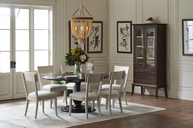 Classic dining room with a dark wood round pedestal table, upholstered dining chairs, and a glass-front cabinet, adorned with botanical artwork and a bead chandelier.