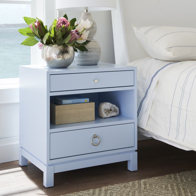 Light blue wooden nightstand with a drawer and open storage, featuring a decorative lamp and floral arrangement on top.