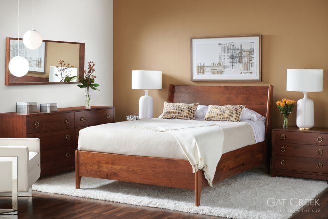 Bedroom with a rich, cherry wood bed frame and matching wood dressers, complemented by modern white lamps and a cozy rug.