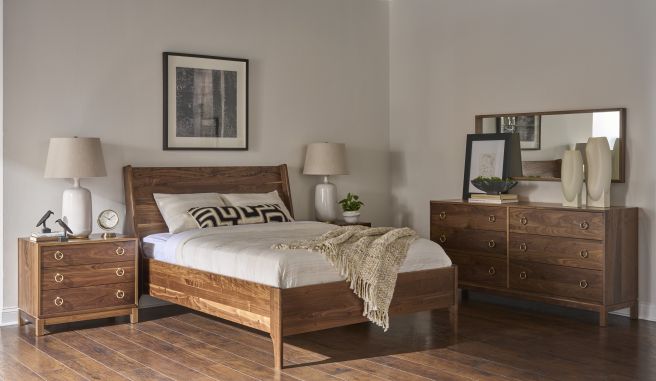 Solid walnut wood bed, nightstand, and dresser set in a primary bedroom, with simple bedding, lamps, and wall art on hardwood floors.